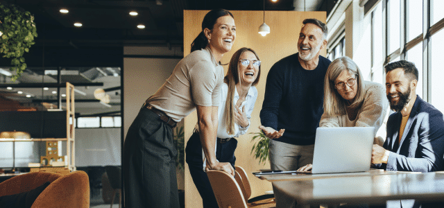 
An energetic moment of teamwork in the office, where a diverse group of professionals are reviewing and discussing at a laptop. This image reflects our core values and commitment to customer service across our three countries of operation.