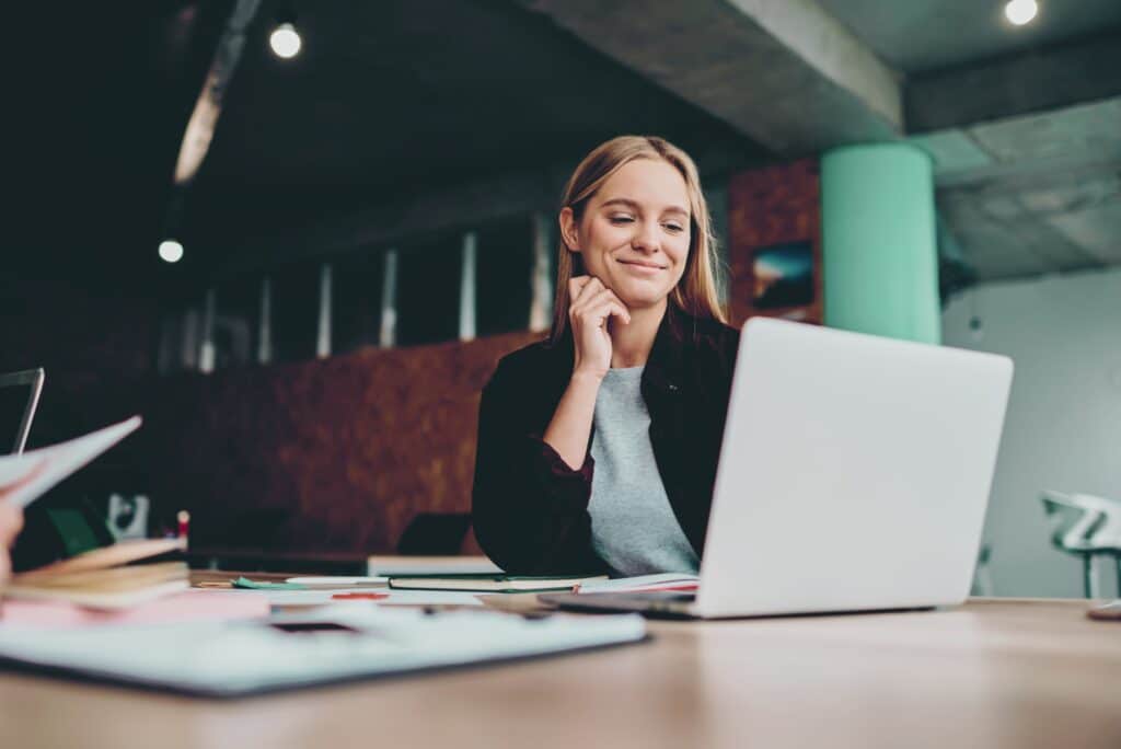 A smiling woman working at a laptop in an office, embodying the values of OPR-Finance: responsible, customer-oriented, and progressive. She represents the company's commitment to the well-being of its staff and clients as a part of its business financing solutions.